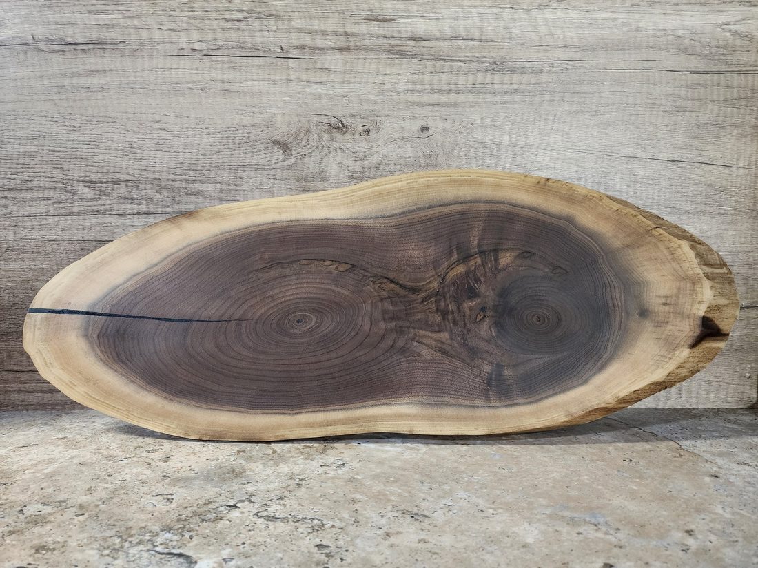 Oval live-edge charcuterie board cut from a single walnut slab showing natural growth rings
