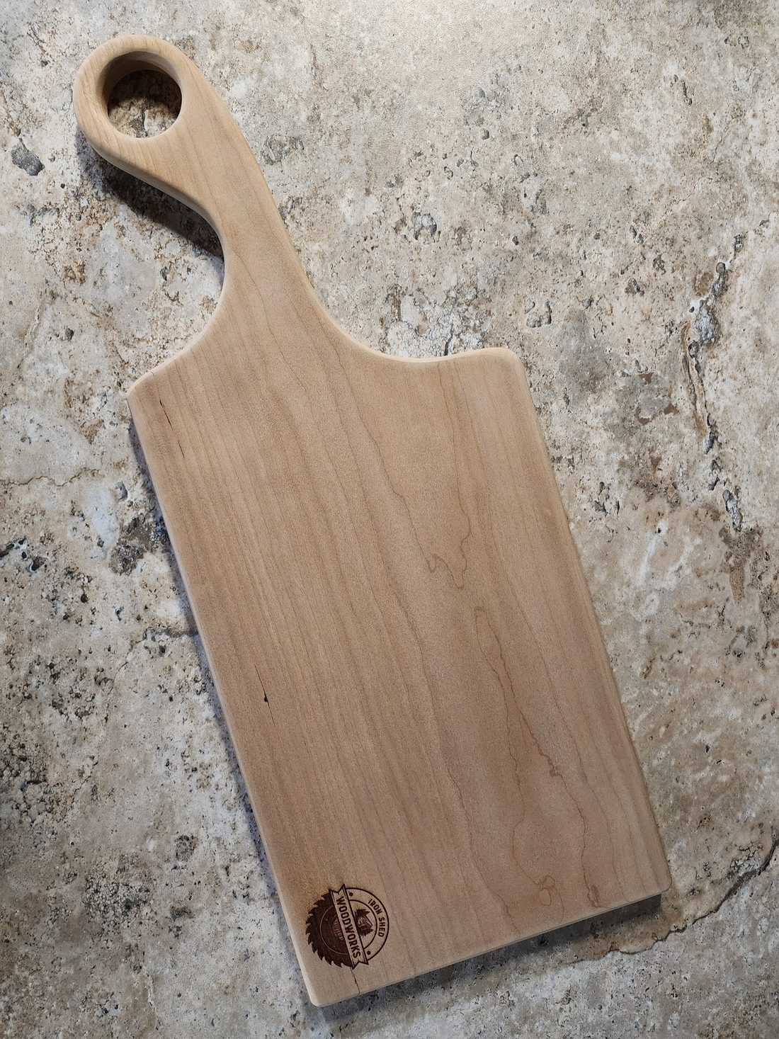 Cherry and maple paddle-style cutting board with a carved hanging handle